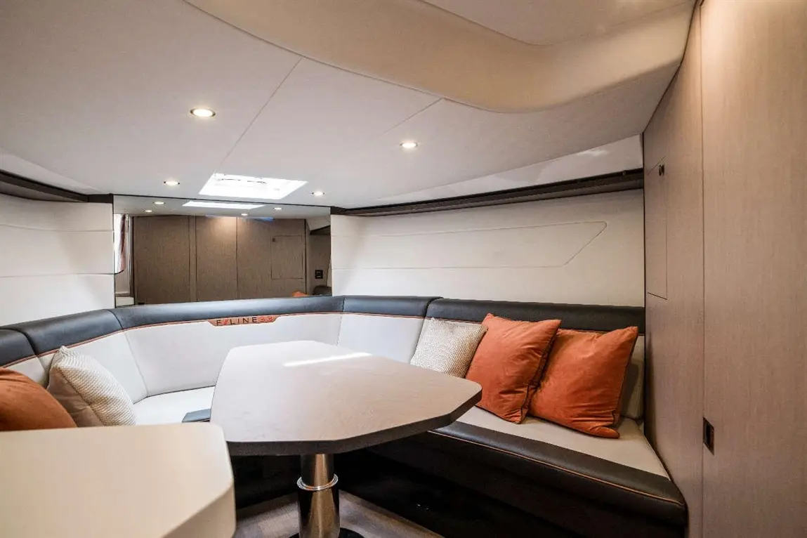 Luxury yacht interior with a curved leather seating area, orange cushions, and a sleek table under soft LED lighting.